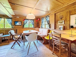 A cozy cabin interior with a wooden dining table, chairs, a white sofa, and a large window with curtains. - Winterberg by Interhome (Feldberg)