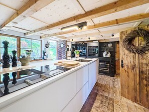 A modern kitchen with a central island, wooden beams on the ceiling, and a view of the outdoors through large windows. - Winterberg by Interhome (Feldberg)