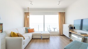 A modern living room with a sofa, ottoman, and a TV on a wooden stand. - Westcliff I with seaview by Interhome (Blankenberge)
