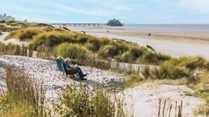 A sandy beach with a person sitting on a chair, a pier in the background, and a building near the water. - Westcliff I with seaview by Interhome (Blankenberge)