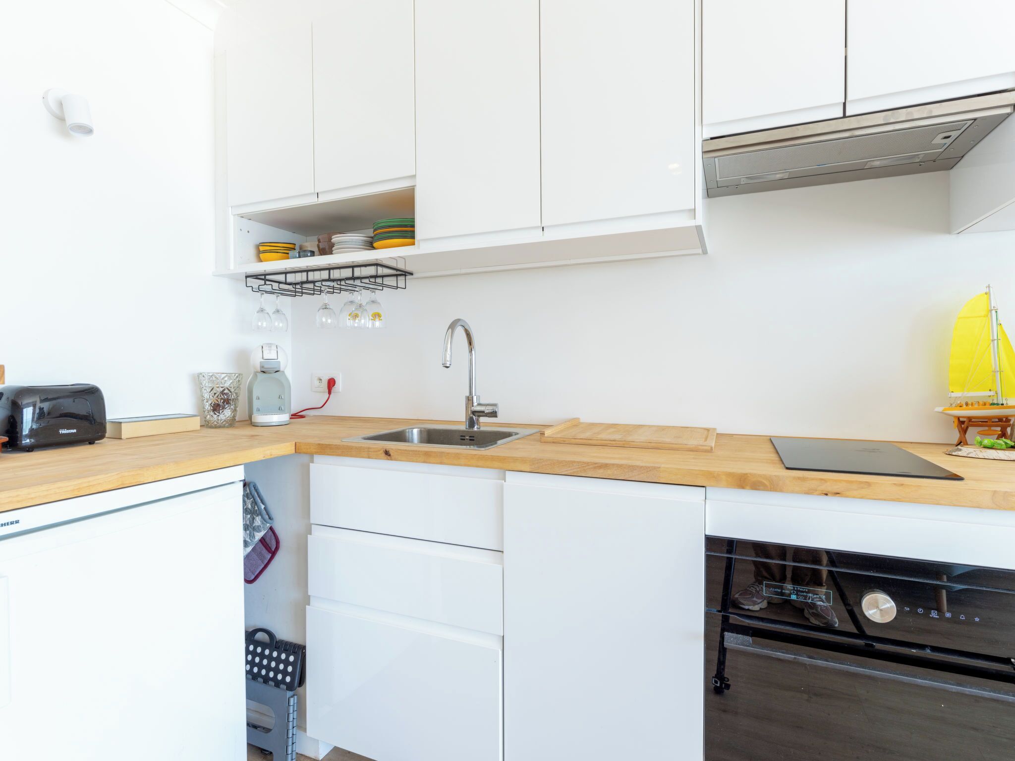 A modern kitchen with white cabinets, a wooden countertop, a sink, a toaster, and a small sailboat model.