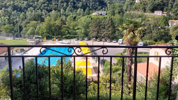 A view of a swimming pool with a mountain backdrop, surrounded by lush greenery and a few buildings. - STUDIO FOR RENT IN PRATS DE MOLLO, Pyrénées-Orientales.  THE MOST BEAUTIFUL VILLAGE IN FRANCE.  (Prats-de-Mollo-la-Preste)