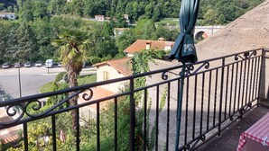 A balcony with a view of a hillside, a parked car, and a building with a red roof. - STUDIO FOR RENT IN PRATS DE MOLLO, Pyrénées-Orientales.  THE MOST BEAUTIFUL VILLAGE IN FRANCE.  (Prats-de-Mollo-la-Preste)