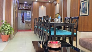 Hall dell'hotel con pannelli in legno, una reception, un'area ristorazione con sedie e tavoli, una pianta in vaso e un soffitto con illuminazione a incasso e elementi decorativi.
