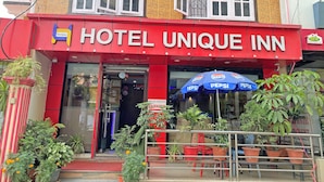 Un hotel chiamato "Hotel Unique Inn" con una facciata rossa, diverse finestre e un ombrello con il marchio Pepsi.