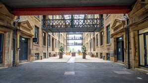 Une cour intérieure abritée, avec une allée centrale, entourée de bâtiments en briques portant l’inscription « Entrepôt », et des plantes en pot placées dans les coins.