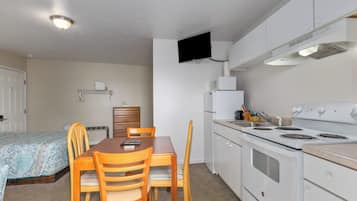 A compact kitchen with a stove, microwave, and a flat-screen TV mounted on the wall.