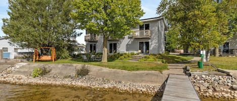 A two-story house with a balcony, a wooden deck, and a small pond.