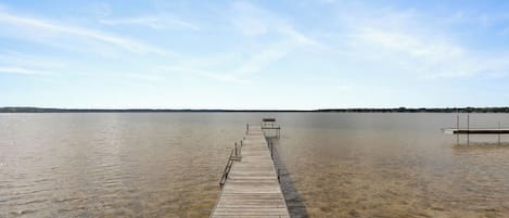 A wooden pier extending into a calm lake with clear water, surrounded by a flat landscape.