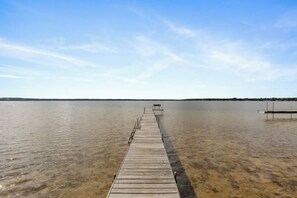 Eine hölzerne Mole erstreckt sich über einen ruhigen See mit klarem Wasser, umgeben von einer flachen Landschaft.