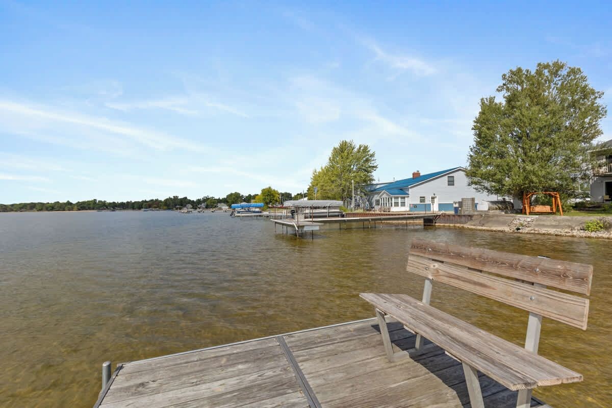 A wooden dock extending into a calm lake with a bench in the foreground.
