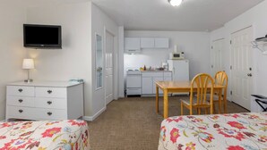 Ett kompakt hotellrum med en säng, ett skrivbord, en stol, en TV, ett litet kök och ett badrum.