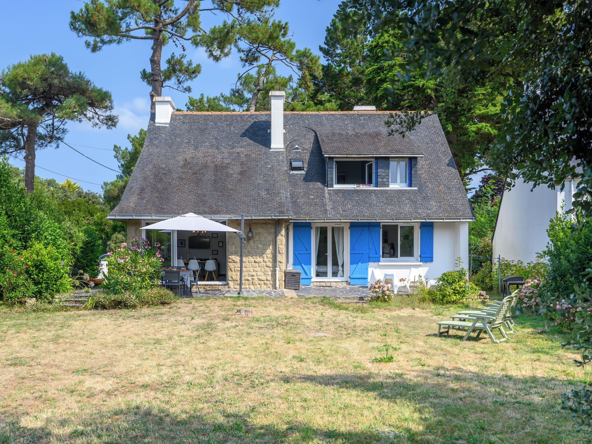 A two-story house with a stone facade, blue shutters, and a grey roof.