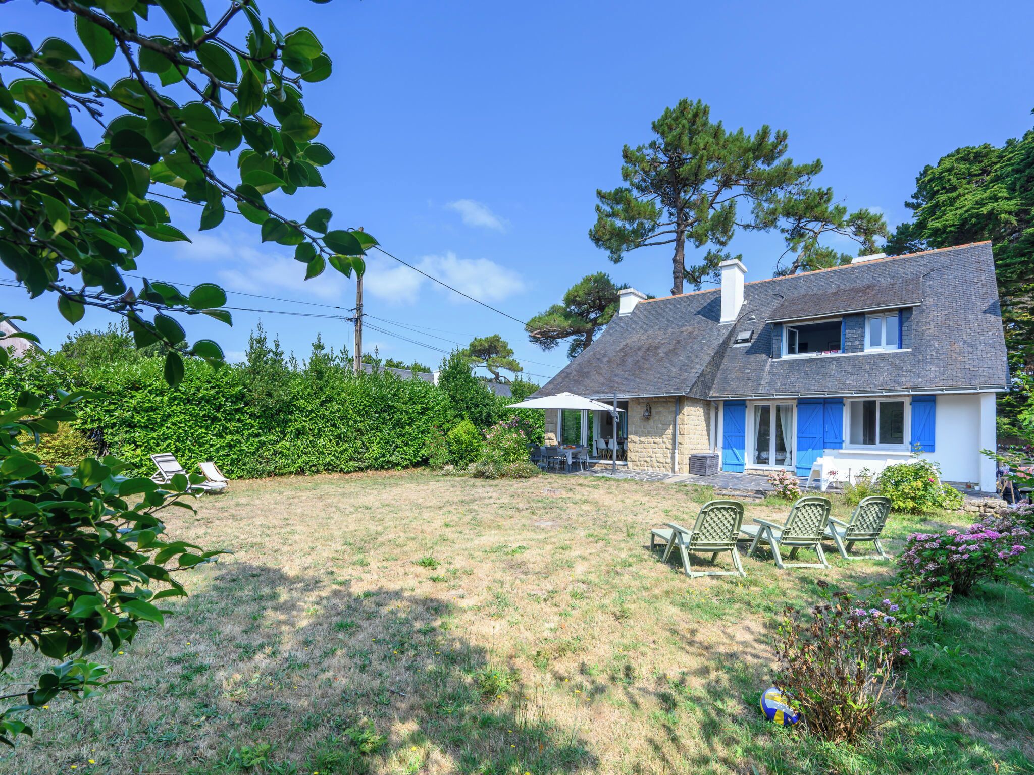Ein zweistöckiges Haus mit Steinverkleidung, einem geneigten Dach und einer kleinen Terrasse mit Gartenmöbeln.