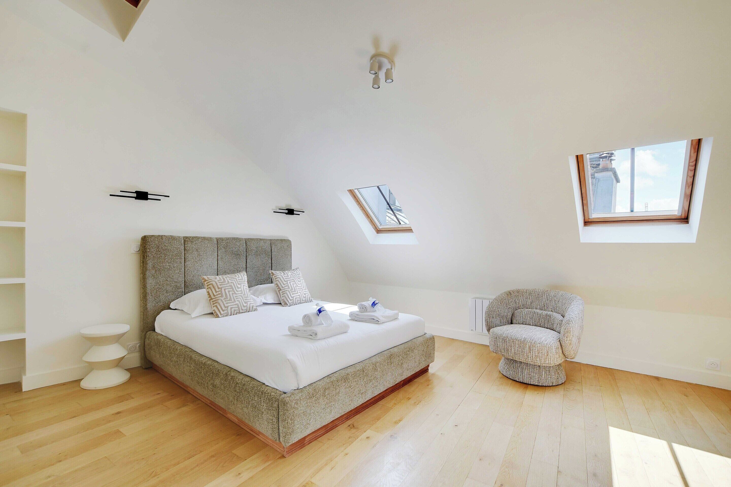 A bedroom with a large bed, a chair, a skylight, and a ceiling fan.
