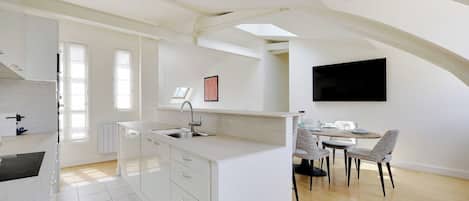 Uma cozinha moderna com armários brancos, uma ilha central e uma área de refeições com mesa e cadeiras.