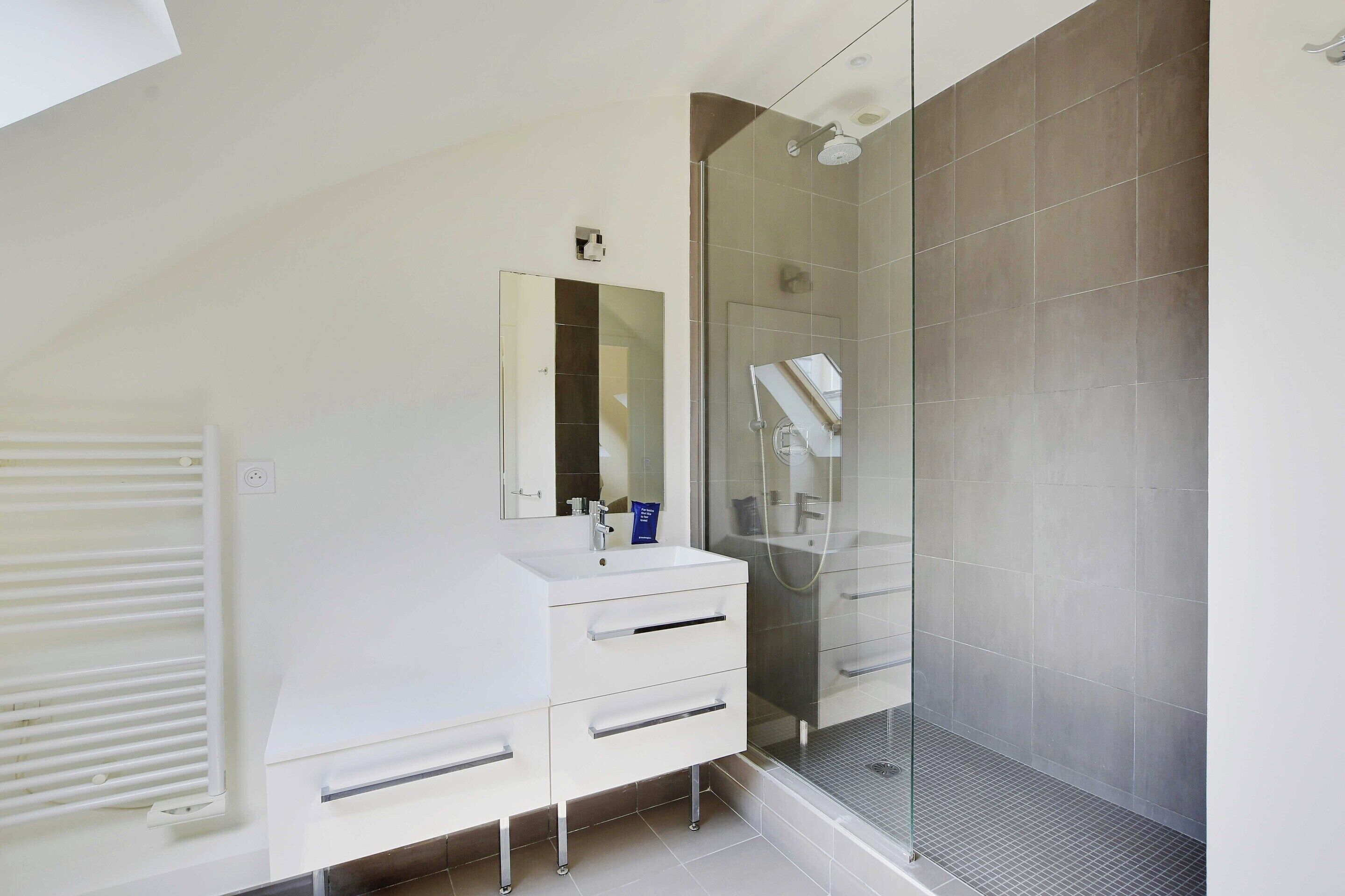 A modern bathroom with a white vanity, a glass shower enclosure, and a large mirror.
