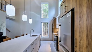 Una cocina moderna con una isla central, luces colgantes, una estufa integrada y un amplio ventanal.