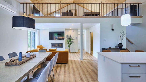 Amplia sala de estar con techo alto, suelo de madera y zona de comedor con una mesa larga y sillas.