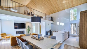 Un interior moderno con zona de comedor, cocina y un altillo con techo de madera.