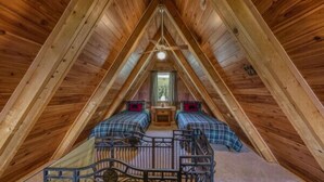 An attic bedroom with two beds, a ceiling fan, and a small window.