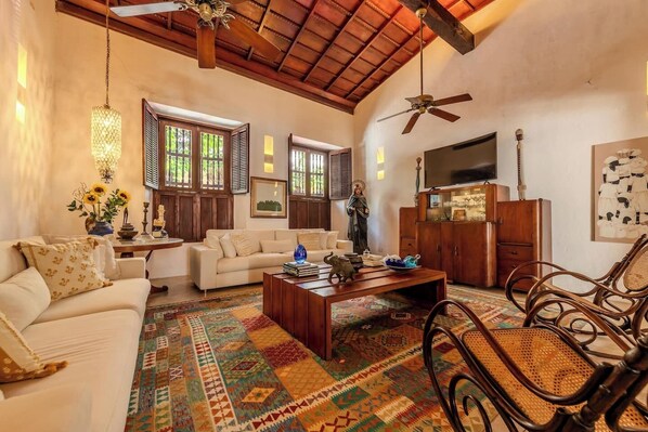 A spacious living room with a high ceiling, a large window, and a ceiling fan.