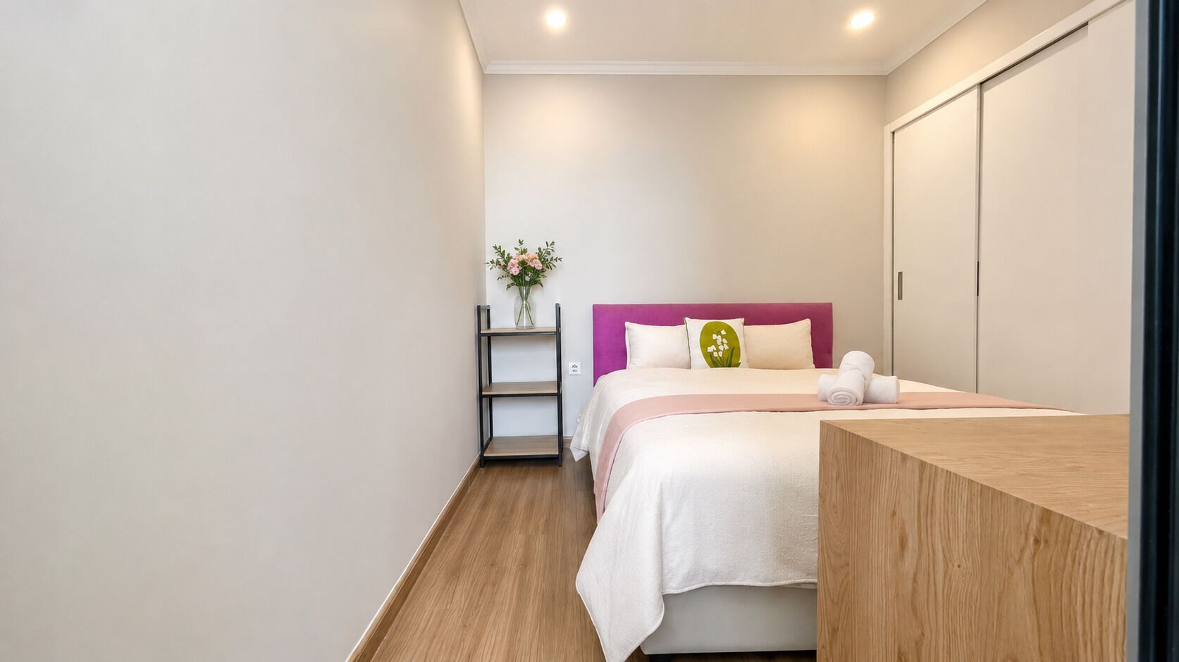 Quarto com cama, mesa de cabeceira, prateleira com um vaso e guarda-roupa.
