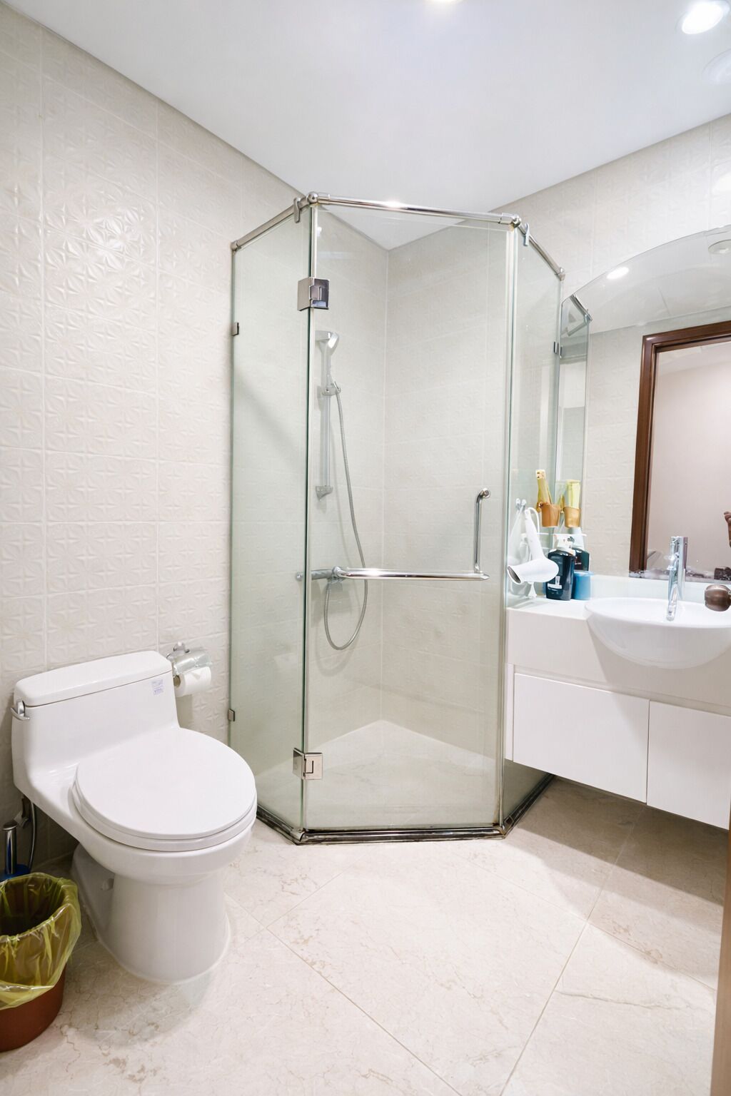 Un baño moderno con ducha envuelta en vidrio, inodoro y lavamanos con artículos de aseo.