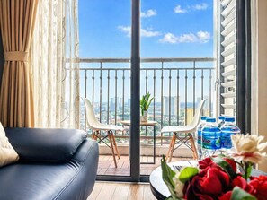 En balkon med udsigt over byen, en lædersofa, et lille bord med en potteplante og vand på flaske.