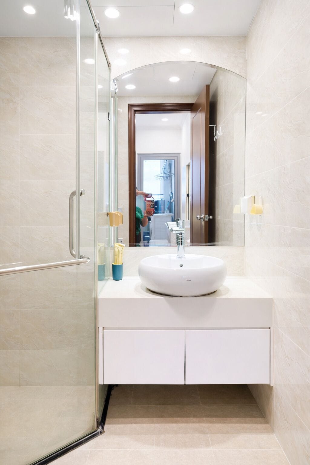 Een moderne badkamer met een douchecabine van glas, een witte wastafel en een spiegel.