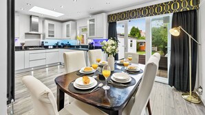 A modern kitchen with white cabinets, a dining area with a dark wooden table, and a view of the outdoors through large windows. - 5 Bedrooms house near Wembley StadiumI Free parking I Discounts for Longer Stays (Wembley)