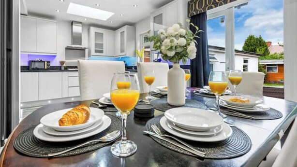 A breakfast table set with croissants, orange juice, and plates, in a modern kitchen with white cabinets and a view of the outside. - 5 Bedrooms house near Wembley StadiumI Free parking I Discounts for Longer Stays (Wembley)