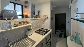 A modern kitchen with a gas stove, a toaster, and a sink. There are various kitchen items on the counter, including a vase and spice jars.
