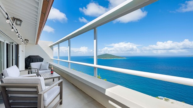 Ein Balkon mit Blick auf das Meer und eine kleine Insel. Esstisch mit Flasche und Gläsern, sowie ein überdachter Grill.