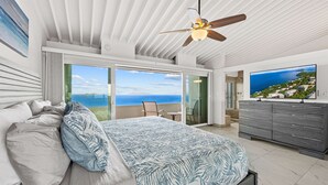 Ein Schlafzimmer mit Bett, Deckenventilator, Fernseher und einem Balkon mit Meerblick.