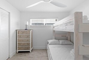 A bunk bed room with a ceiling fan, a dresser, and a window with blinds.