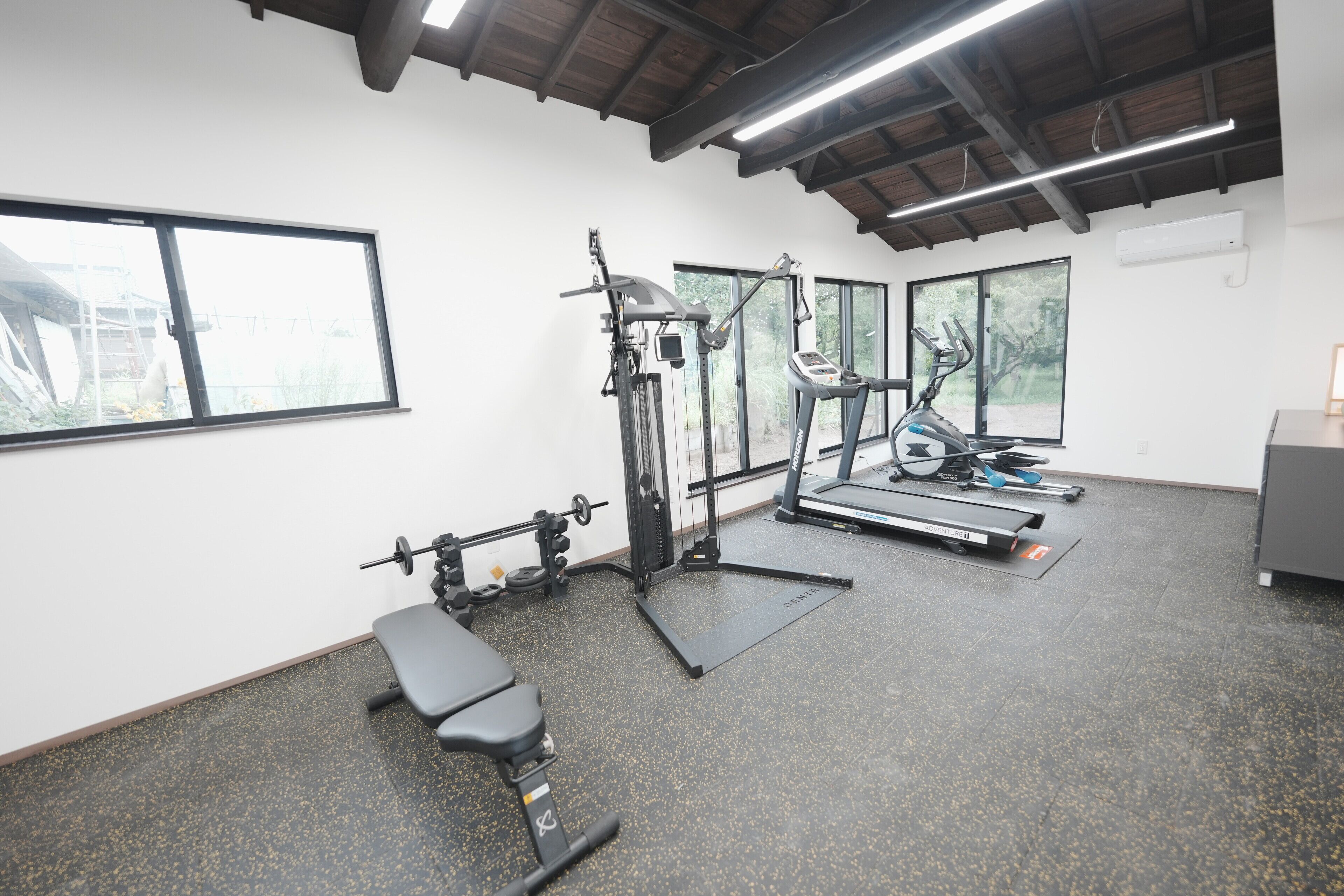 Une salle de sport équipée d’un banc, d’un banc de musculation, d’un tapis de course et d’un vélo d’exercice.