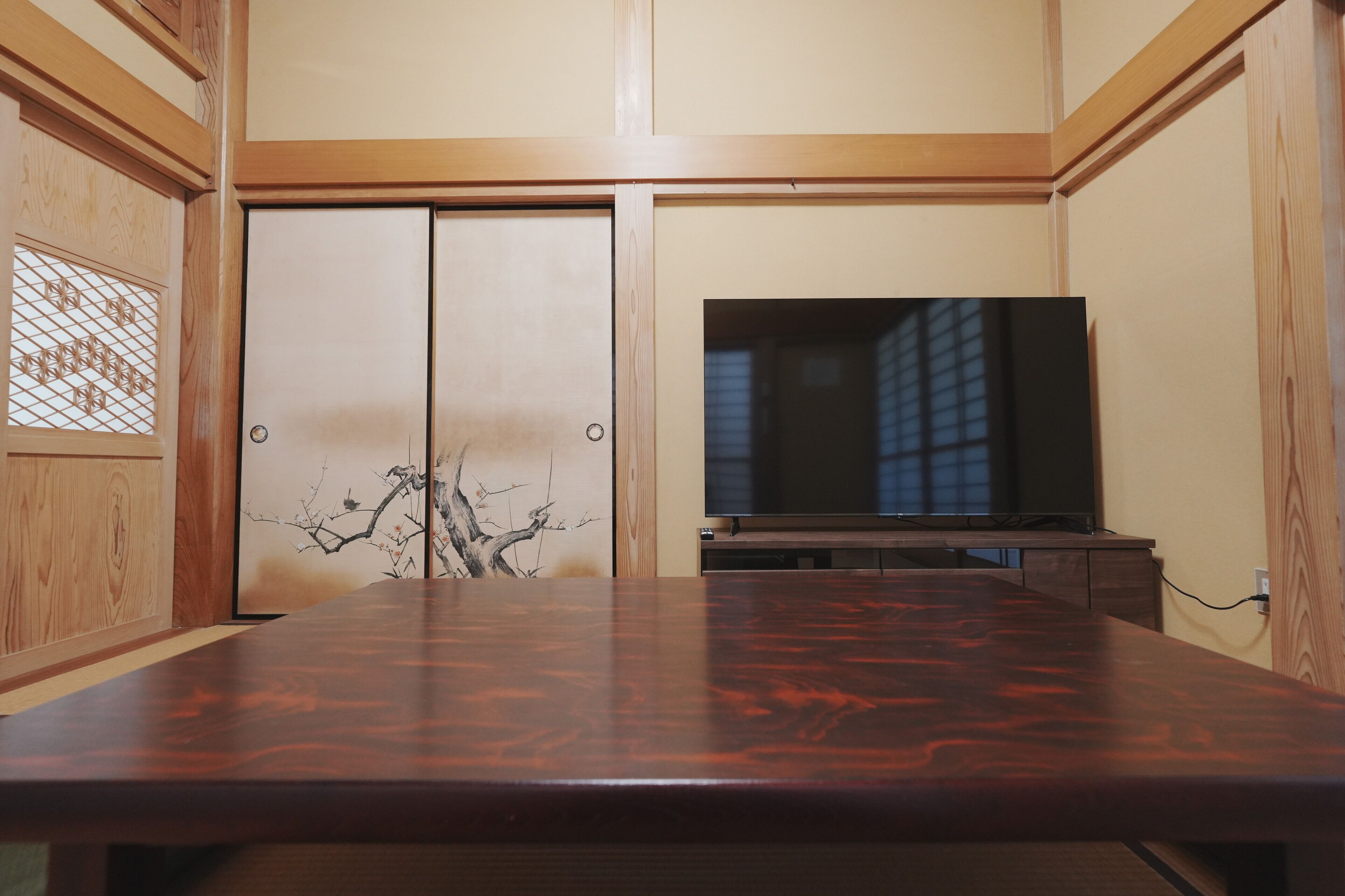 A room with a wooden table, a television on a stand, and sliding doors with a decorative panel.