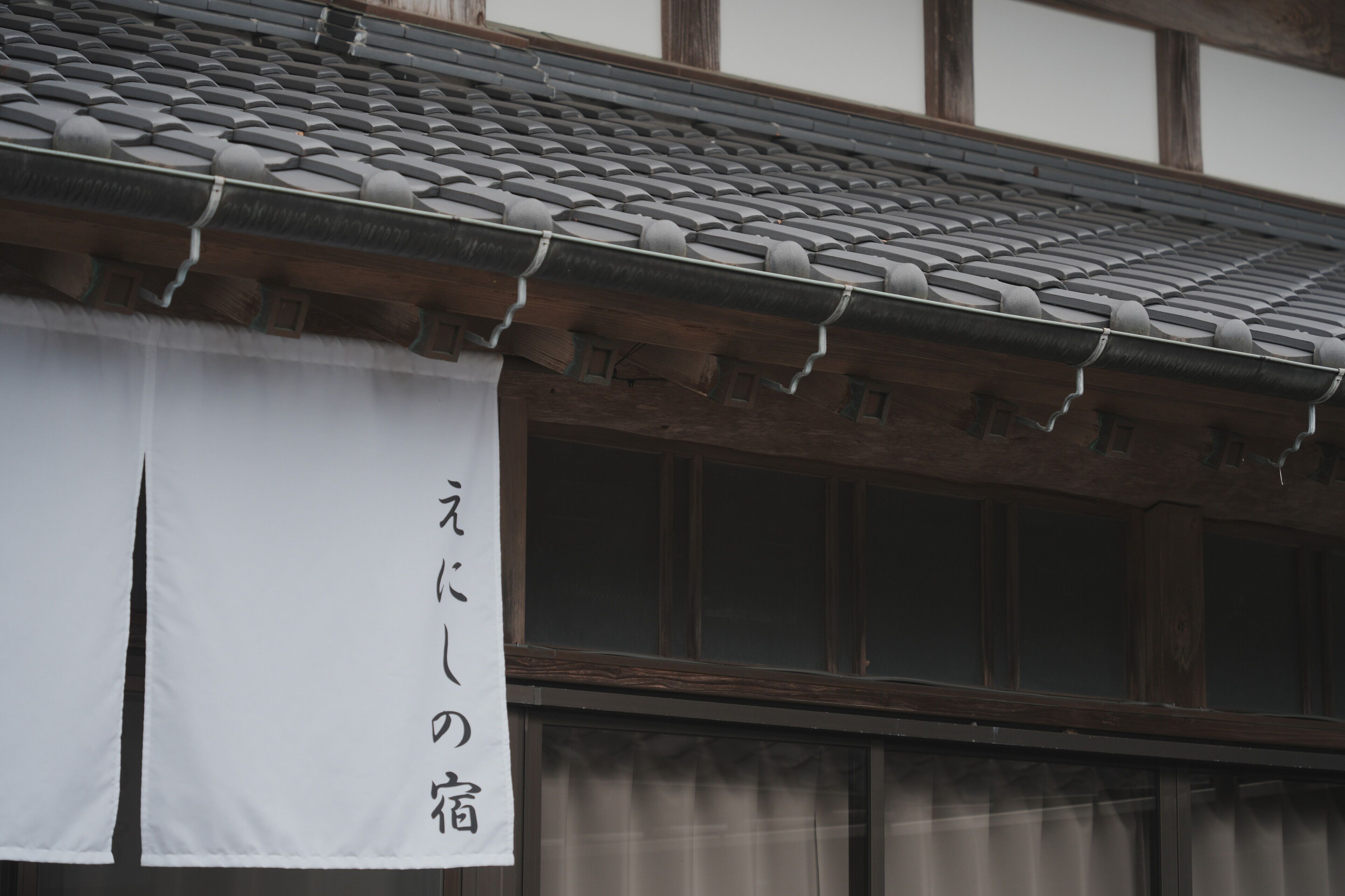 Un edificio japonés tradicional con tejado de tejas y una pancarta blanca con caracteres japoneses.