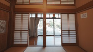 Una habitación japonesa tradicional con suelo de tatami, puertas correderas y vistas a un jardín.
