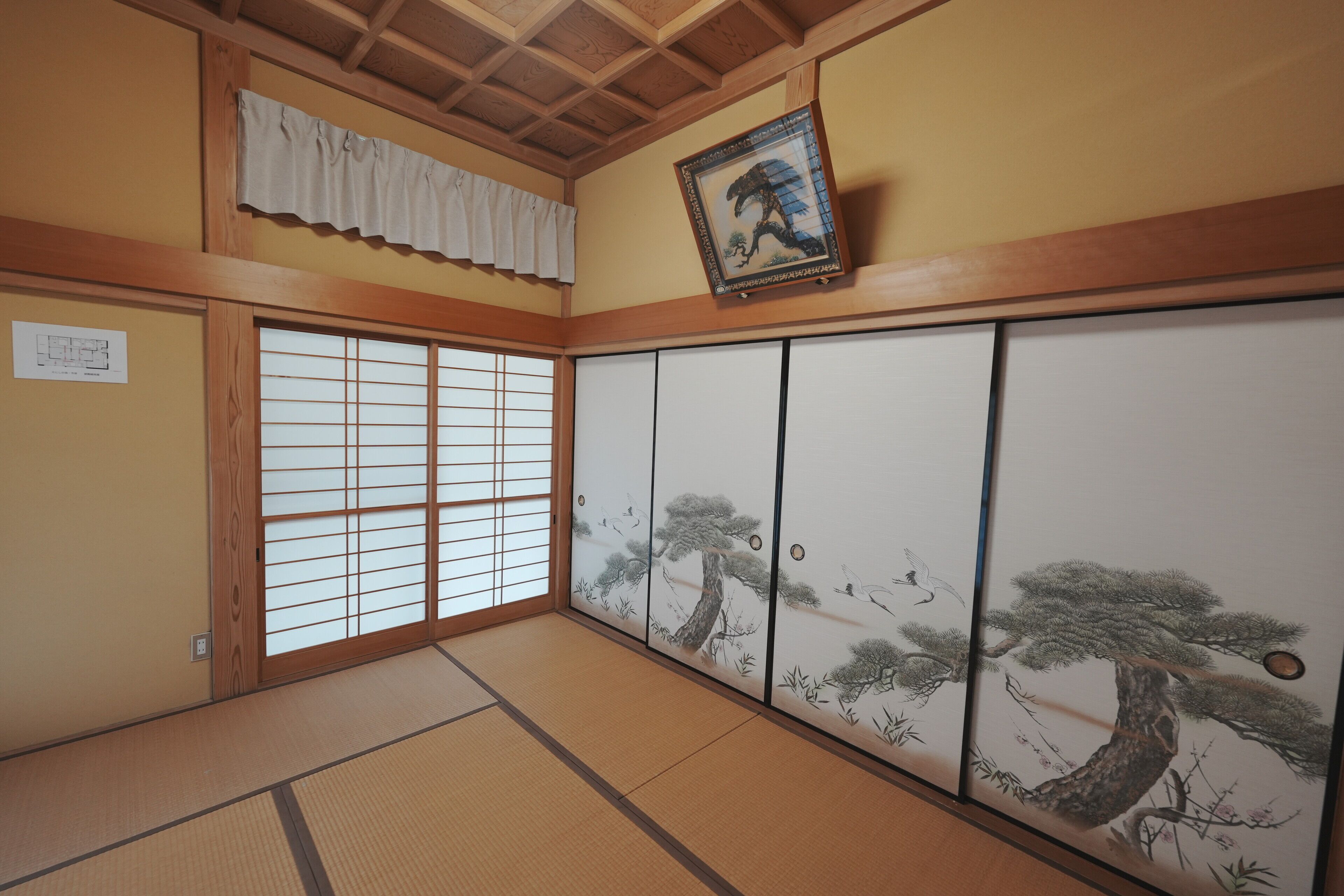 Una habitación tradicional japonesa con suelo de tatami, puertas correderas shoji y una obra de arte enmarcada en la pared.