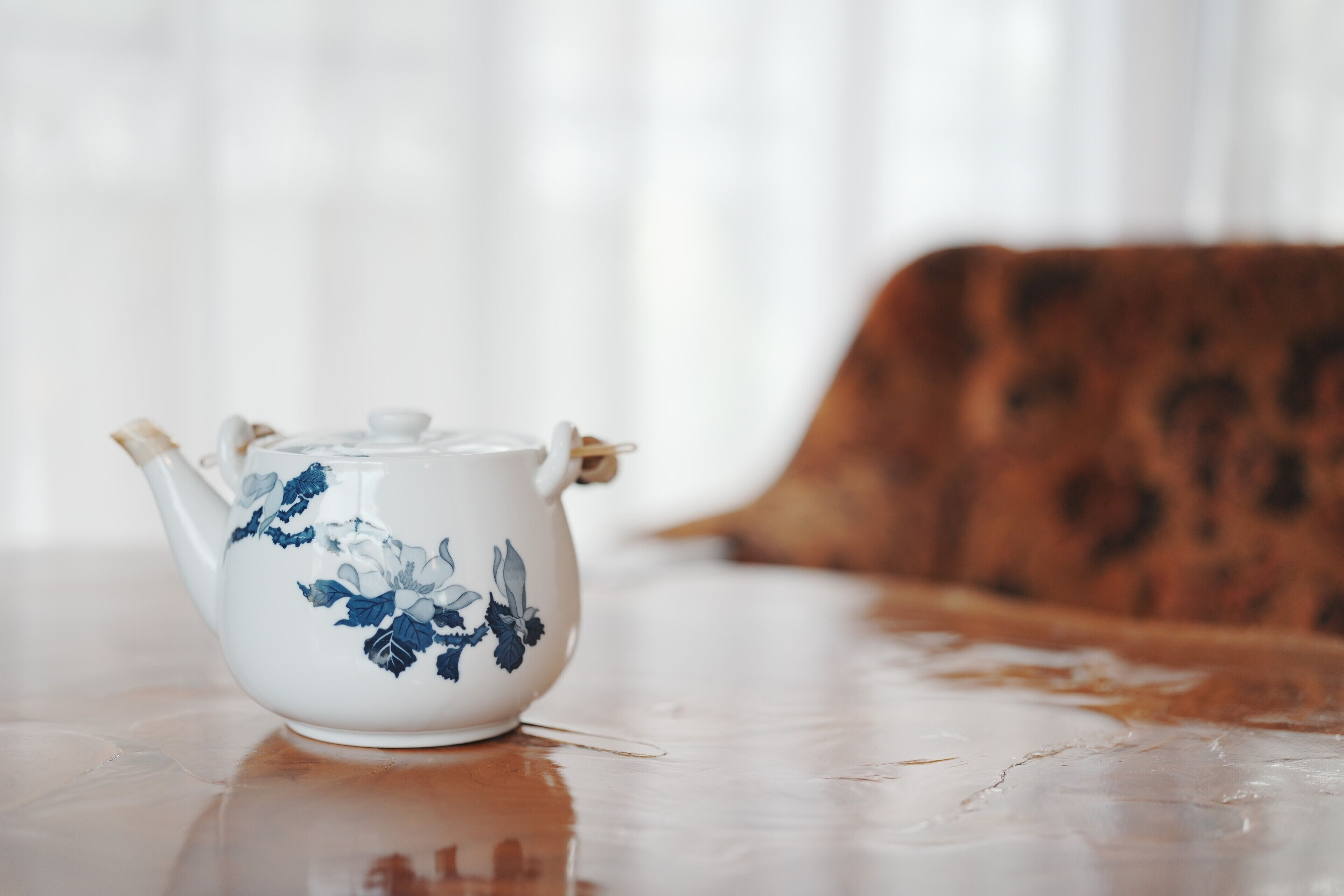 A white teapot with blue floral designs on a wooden table.