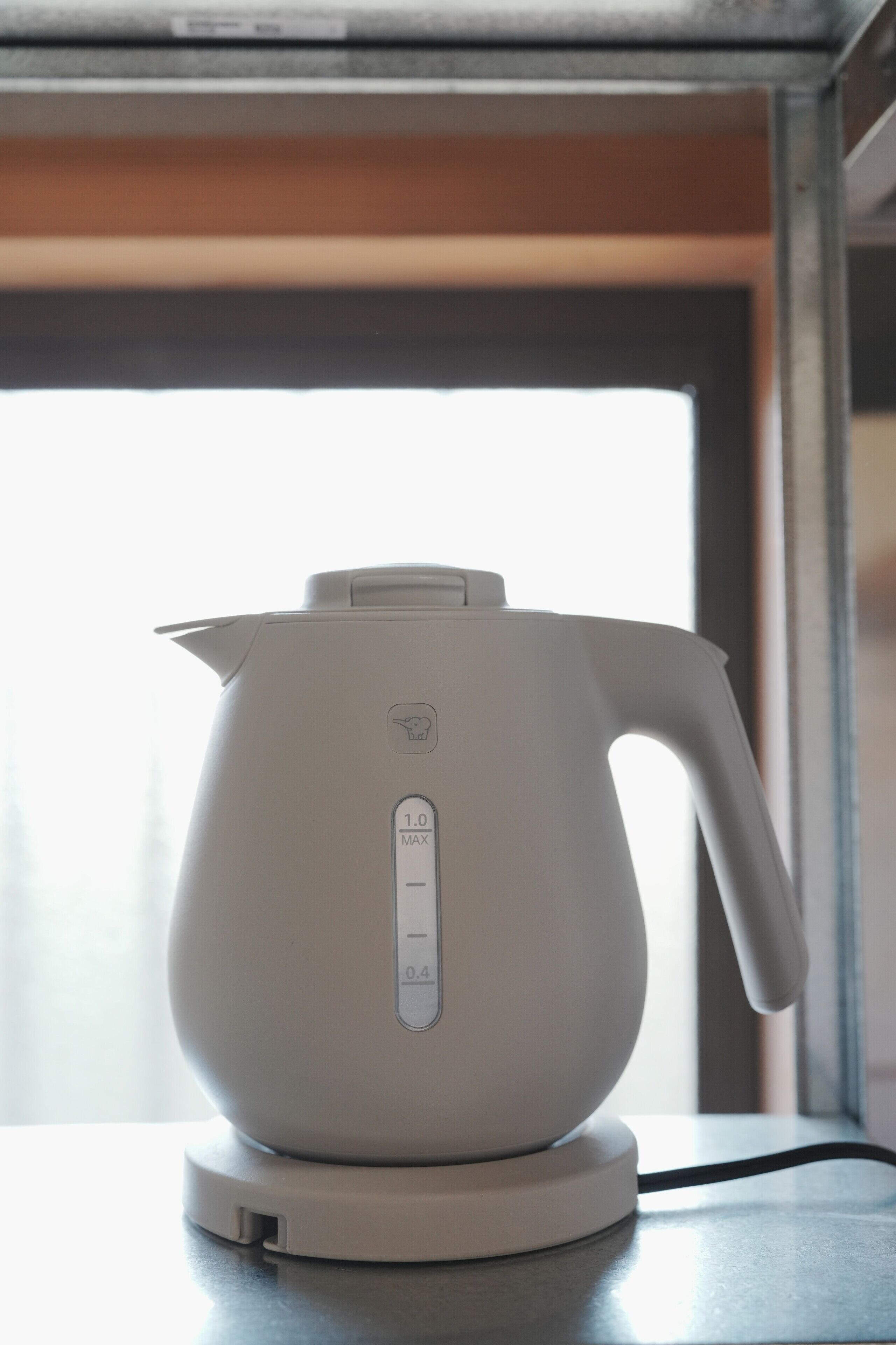 Een witte elektrische waterkoker op een tafel, met een raam op de achtergrond.