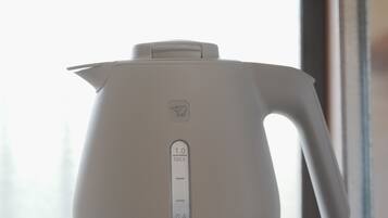 Een witte elektrische waterkoker op een tafel, met een raam op de achtergrond.