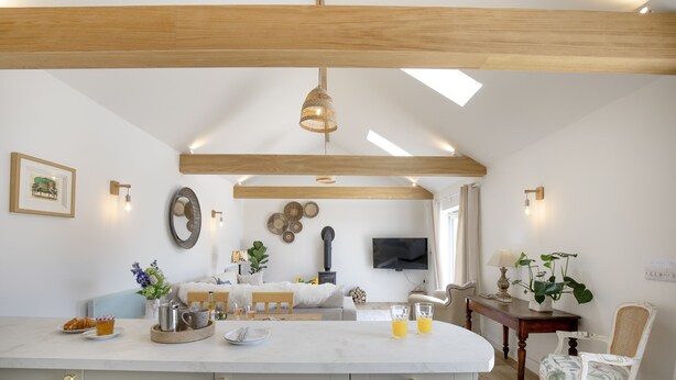 Una cocina moderna con una isla central, vigas de madera, un televisor de pantalla plana y una zona de comedor con mesa y sillas.