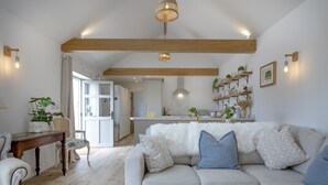 Un salón amplio con un sofá gris, vigas de madera y una cocina al fondo.
