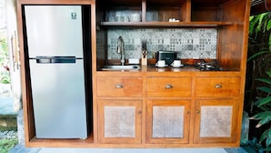 A compact kitchen with a stainless steel refrigerator, wooden cabinets, a tiled backsplash, and a sink. - Tegal Utu Villa (Ubud)