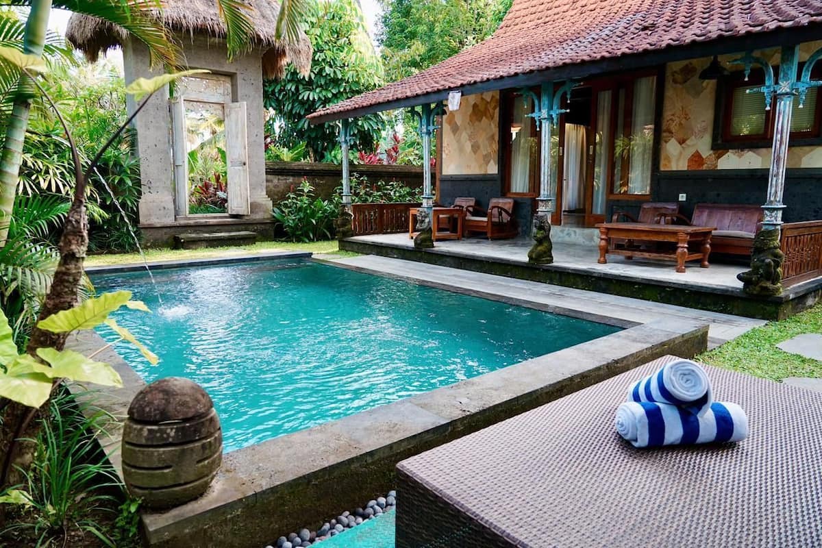 A pool area with a thatched-roof structure, lounge chairs, and a stone barrel.