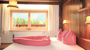 Een kamer met een bed, geruite kussens, een raam met uitzicht op bergen en houten wanden.