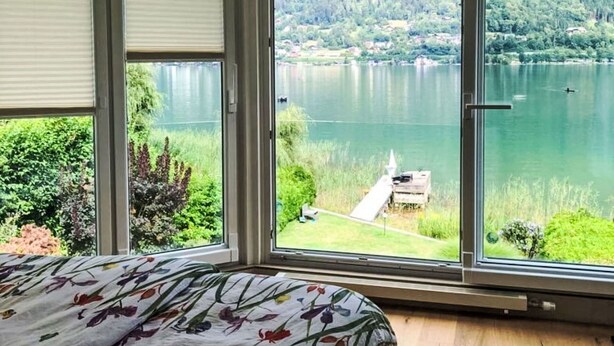 Un dormitorio con un ventanal que da a un lago y colinas boscosas.